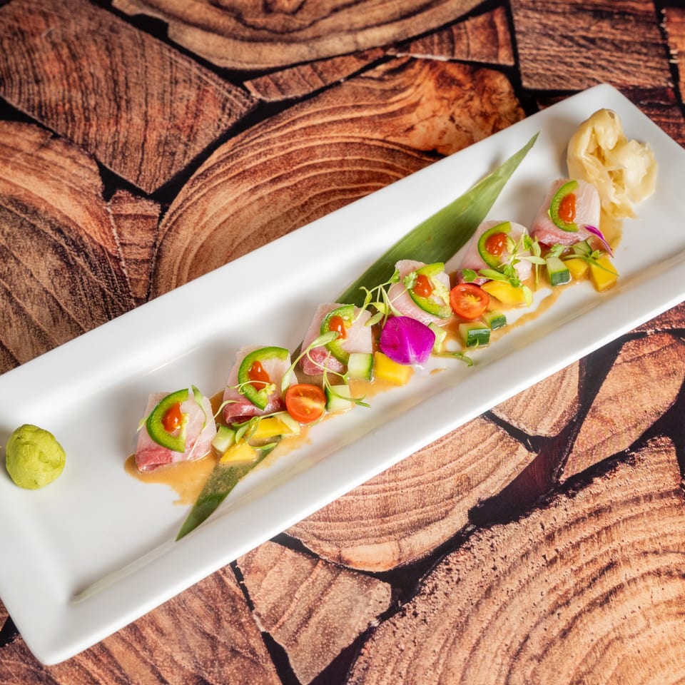 Kenji Sushi's sashimi dish with jalapeños, cherry tomatoes, mango, and cucumber on a white plate.