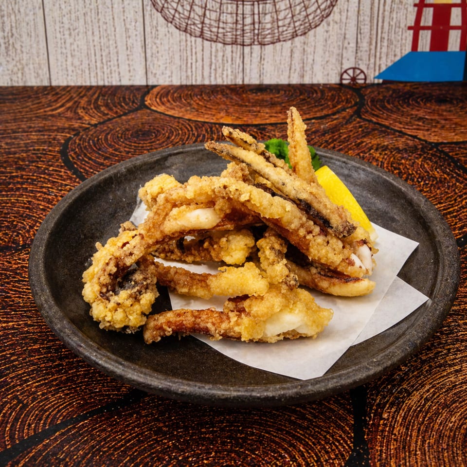 Crispy fried calamari rings and tentacles on a dark plate with a lemon wedge and parsley.