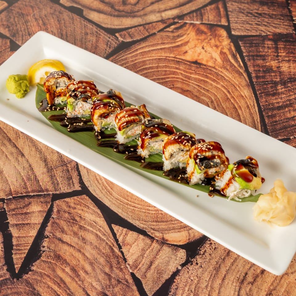 Kenji Sushi's dragon roll with eel, avocado, and sauce, served on a banana leaf.