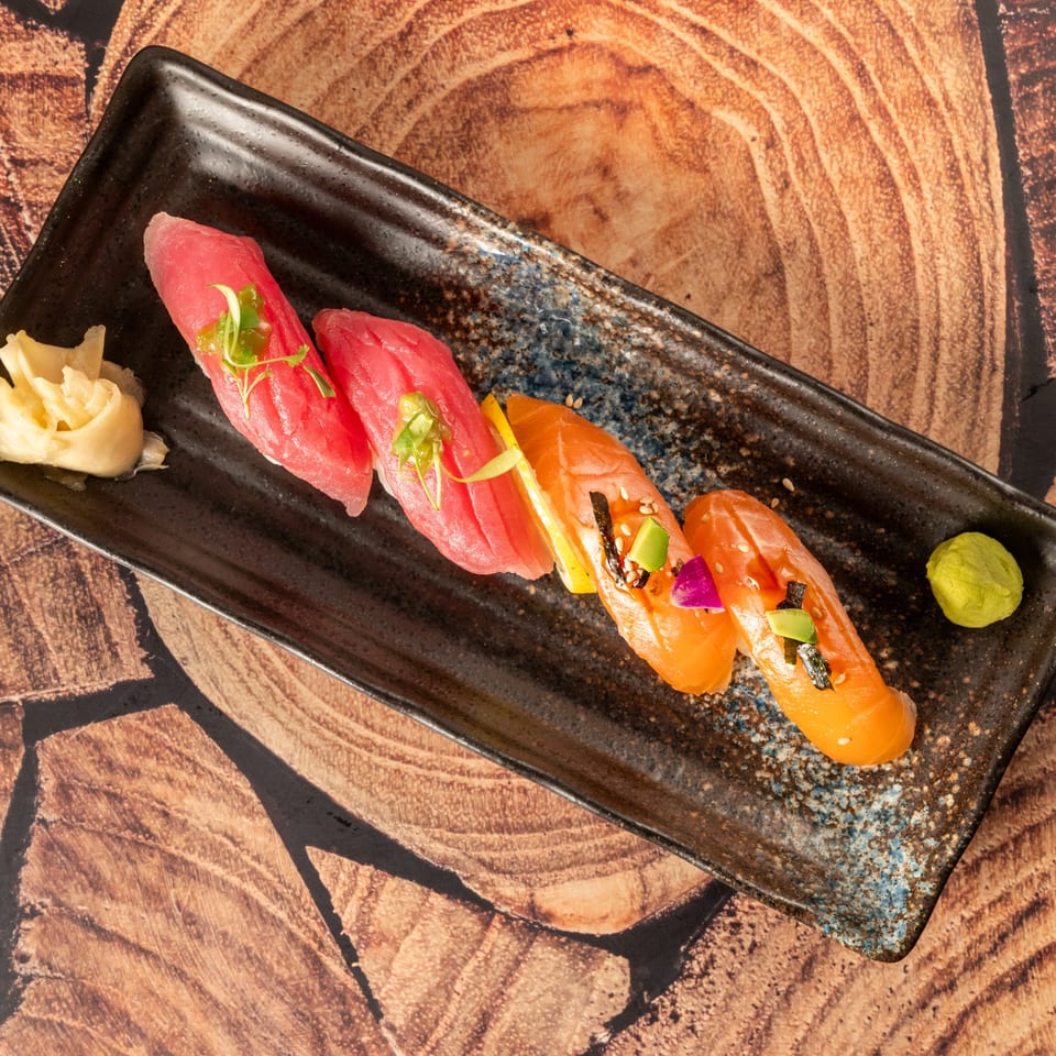 Kenji Sushi's nigiri platter with tuna and salmon sushi, ginger, and wasabi on a black plate.